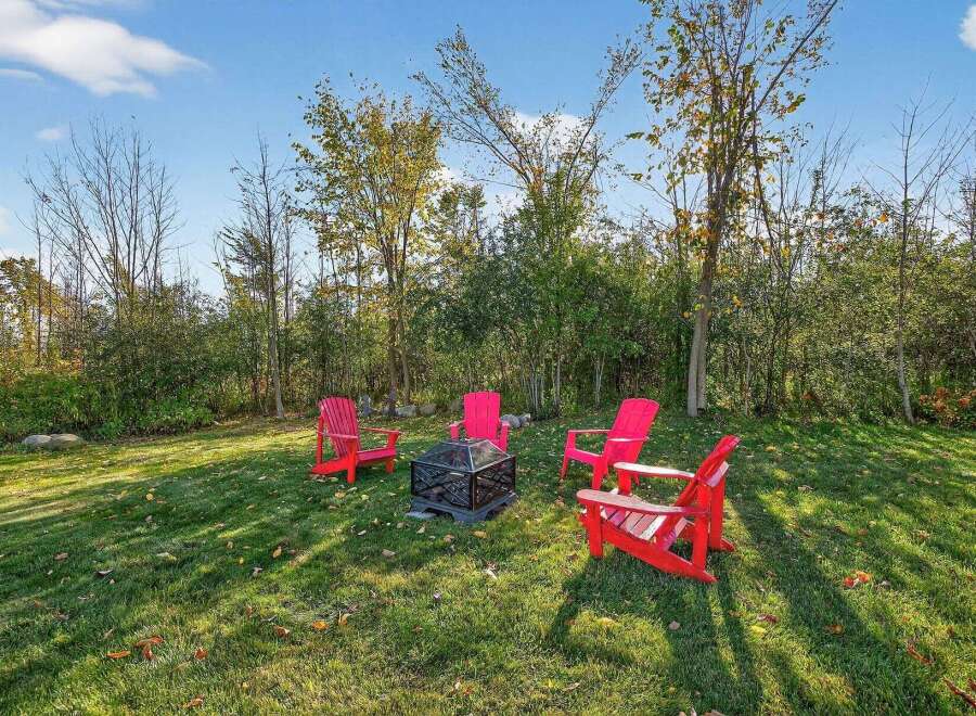Enjoy outdoor living at its finest with this inviting property! Featuring a cozy fire pit surrounded by vibrant red Adirondack chairs, perfect for gatherings.