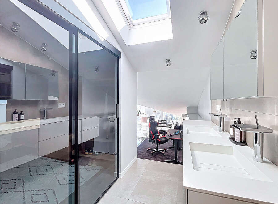This modern bathroom boasts a sleek design with a sliding glass door, a skylight, and a double sink.
