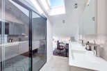 This modern bathroom boasts a sleek design with a sliding glass door, a skylight, and a double sink.