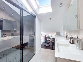 This modern bathroom boasts a sleek design with a sliding glass door, a skylight, and a double sink.