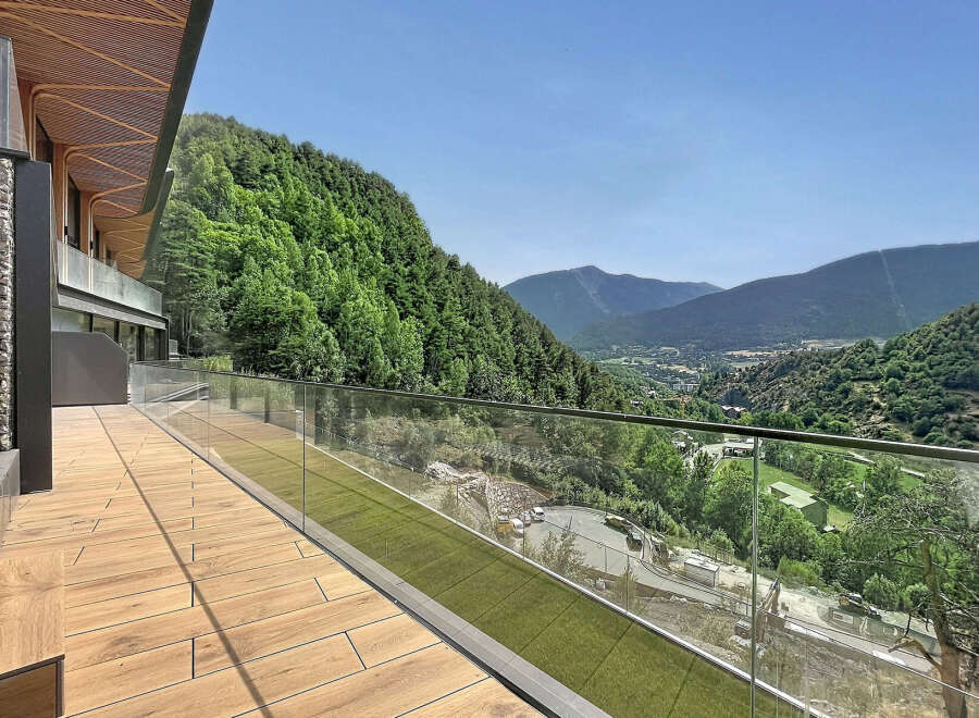 Experience breathtaking mountain views from this modern property featuring a spacious wooden deck and a sleek glass balcony railing.