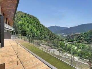 Experience breathtaking mountain views from this modern property featuring a spacious wooden deck and a sleek glass balcony railing.