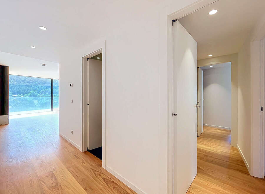 Experience modern living in this spacious hallway featuring elegant hardwood floors and a stunning view of lush greenery through a large window.