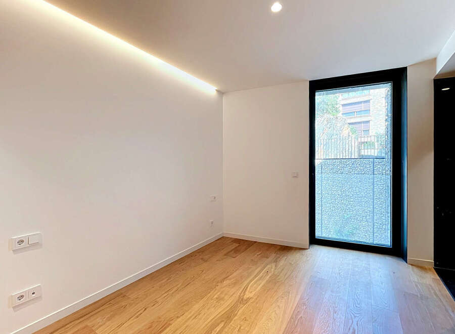 Experience modern living in this bright and airy room featuring a sleek recessed ceiling light and a large window offering natural light.