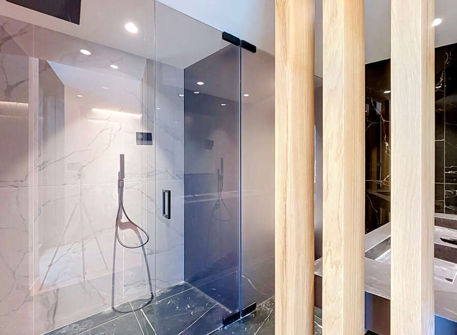 Experience modern luxury in this stunning bathroom featuring a sleek glass-enclosed shower with marble-look tiles and a sophisticated black shower system.