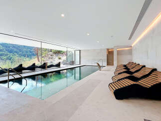 Experience ultimate relaxation in this luxurious indoor swimming pool area, featuring a stunning infinity pool with breathtaking mountain views through expansive floor-to-ceiling windows.