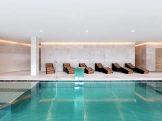 Experience ultimate relaxation in this luxurious indoor pool area, featuring sleek lounge chairs perfect for unwinding.