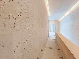 Experience modern luxury in this hallway featuring elegant travertine walls with a unique speckled pattern.