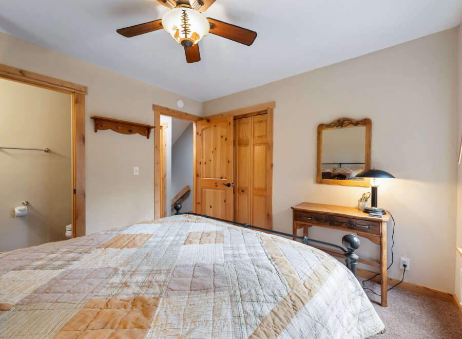 This cozy bedroom features a rustic design with wooden accents and a charming ceiling fan.