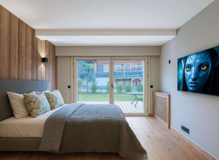 This stunning bedroom boasts a modern design with a touch of nature, featuring a beautiful wooden accent wall and a large glass door that leads to a serene outdoor space.