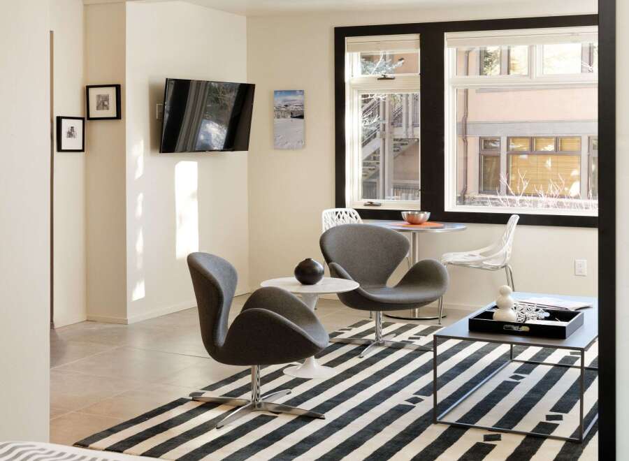 This modern living space features a sleek design with a mounted TV, stylish seating, and a striking black and white striped rug.