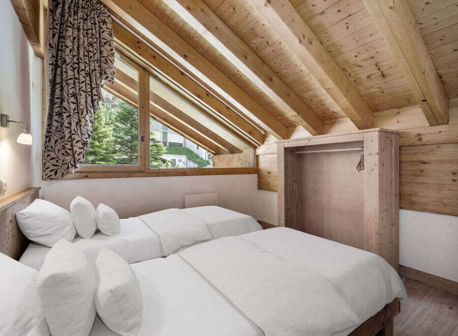 This cozy bedroom features a unique sloped ceiling with exposed wooden beams, creating a warm and inviting atmosphere.