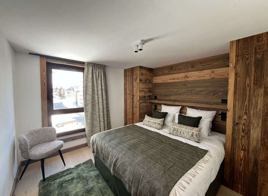Experience luxury living in this stunning bedroom featuring a cozy bed with stylish pillows and a warm, inviting wooden headboard.