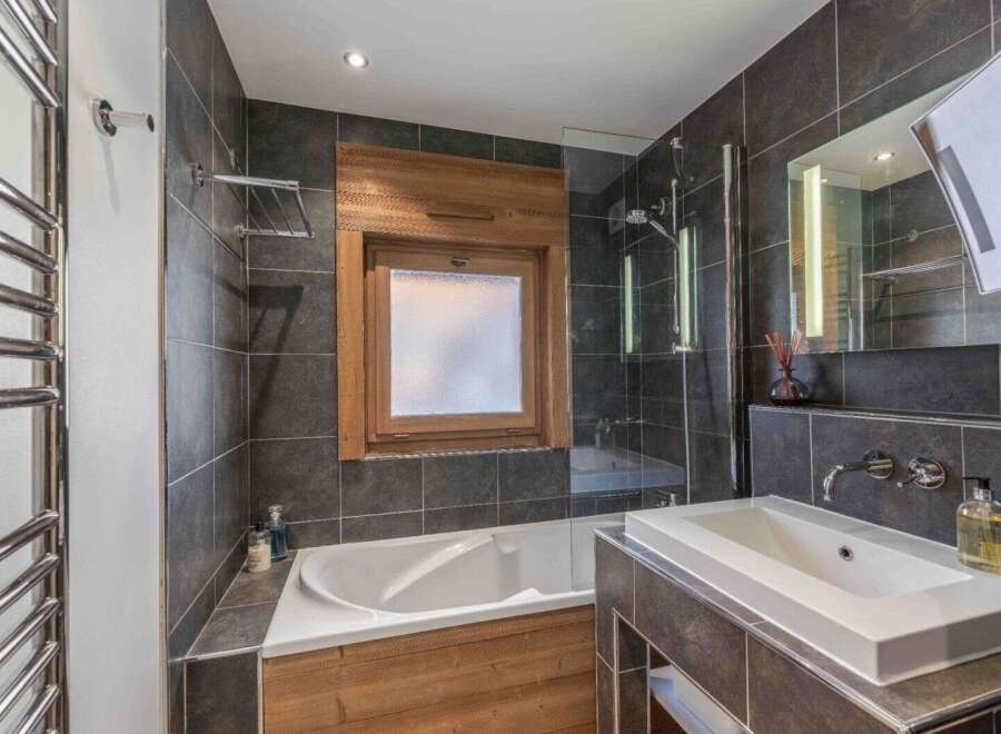 This modern bathroom features a sleek design with dark gray tiles and wooden accents.
