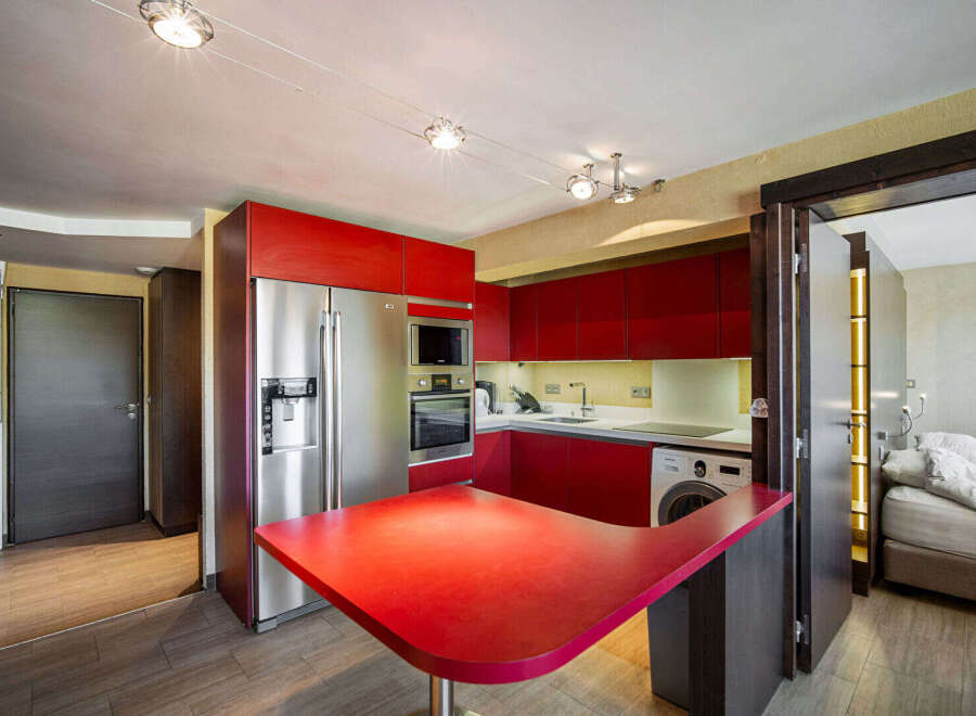 This modern kitchen boasts sleek red cabinetry and stainless steel appliances, creating a stylish and functional space.