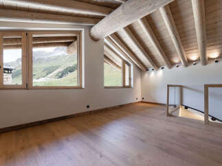 Experience breathtaking mountain views from this stunning attic room, featuring a rustic wooden beamed ceiling and expansive windows.