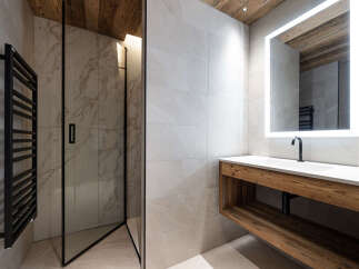 Experience modern luxury in this stunning bathroom featuring a sleek glass-enclosed shower with marble-patterned tiles and a black heated towel rack.