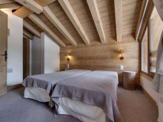 This cozy bedroom features a rustic design with wooden walls and ceiling beams, creating a warm and inviting atmosphere.