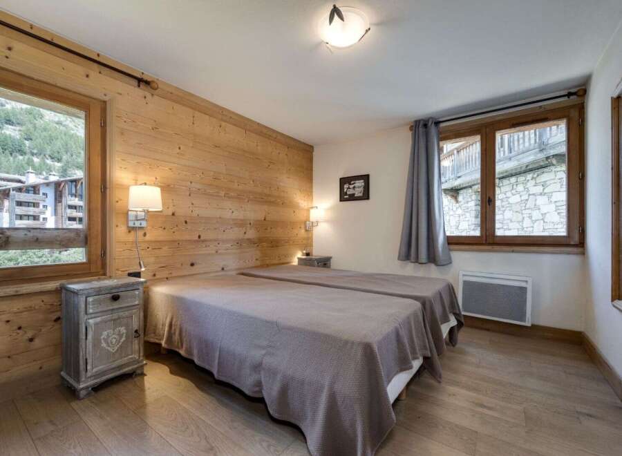 Discover the charm of this cozy bedroom, featuring a rustic wooden wall and elegant twin beds.