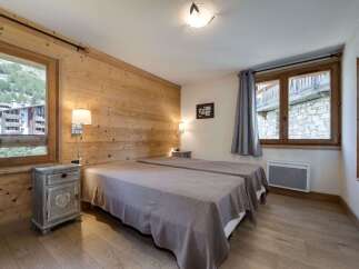 Discover the charm of this cozy bedroom, featuring a rustic wooden wall and elegant twin beds.