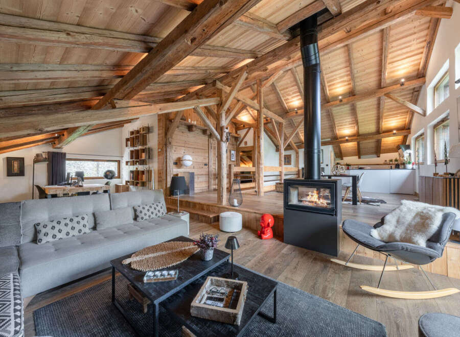 Experience rustic luxury in this stunning mountain chalet living room, featuring exposed wooden beams and a modern fireplace.