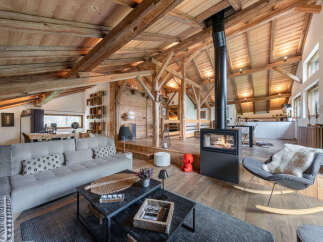 Experience rustic luxury in this stunning mountain chalet living room, featuring exposed wooden beams and a modern fireplace.