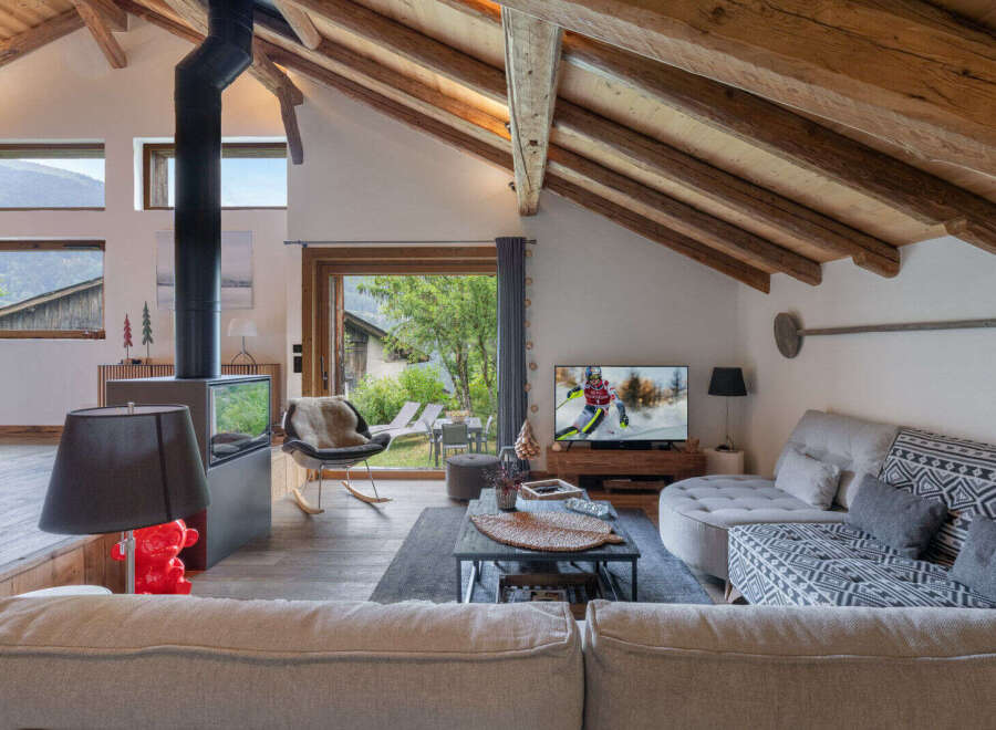 Experience cozy mountain living in this charming chalet featuring a striking black wood-burning stove and exposed wooden beams.