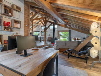 Experience rustic charm and modern comfort in this stunning attic living space, featuring exposed wooden beams and a cozy work area.