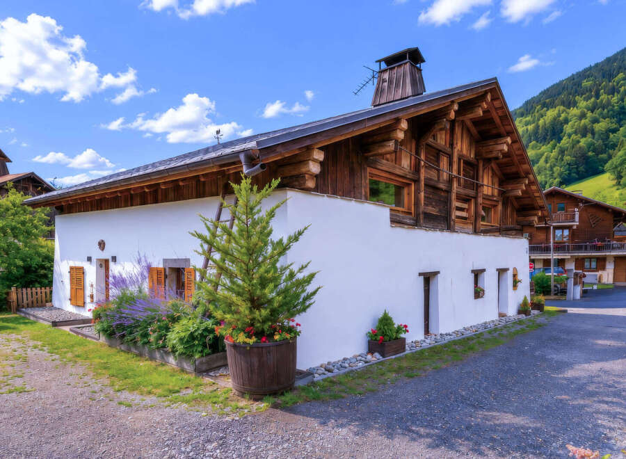 Charming alpine chalet featuring traditional wooden architecture and a bright white facade, nestled against a lush green mountainside.