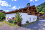 Charming alpine chalet featuring traditional wooden architecture and a bright white facade, nestled against a lush green mountainside.