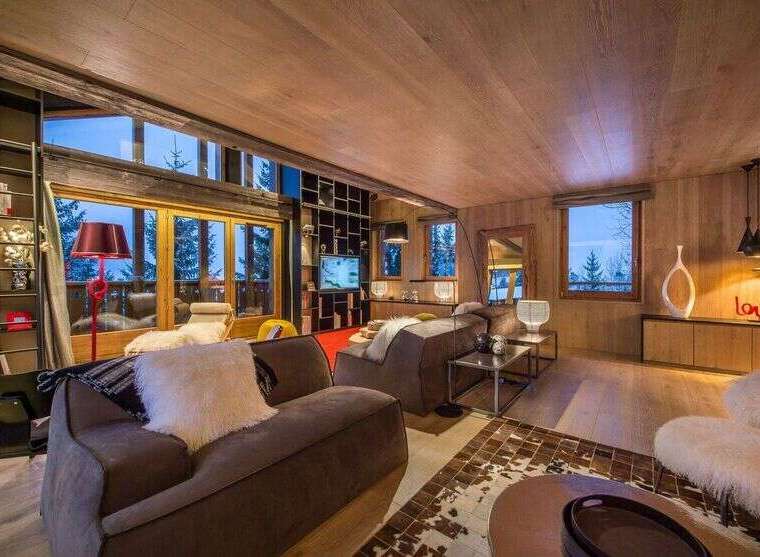 Experience luxury living in this stunning chalet, featuring a cozy living room with a fireplace and large windows offering breathtaking mountain views.