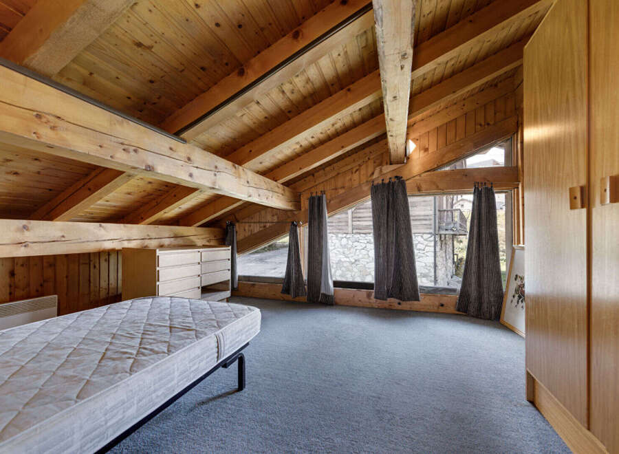 This stunning attic bedroom boasts a unique architectural design with exposed wooden beams and a vaulted ceiling, creating a warm and inviting atmosphere.