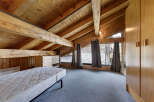 This stunning attic bedroom boasts a unique architectural design with exposed wooden beams and a vaulted ceiling, creating a warm and inviting atmosphere.