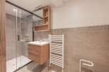 This modern bathroom features a sleek glass shower enclosure, a stylish wooden vanity with a sink, and a convenient wall-mounted mirror cabinet.