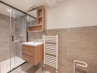 This modern bathroom features a sleek glass shower enclosure, a stylish wooden vanity with a sink, and a convenient wall-mounted mirror cabinet.