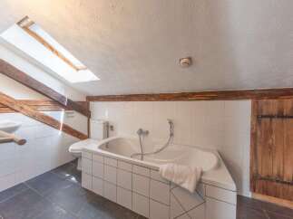 This charming bathroom features a unique design with exposed wooden beams and a skylight, creating a warm and inviting atmosphere.