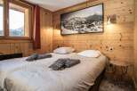 Experience the cozy charm of this bedroom, featuring warm wooden paneling and a stunning mountain view.
