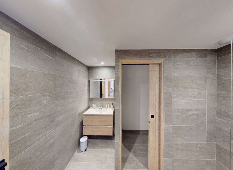 Experience modern comfort in this beautifully appointed bathroom, featuring sleek grey tiled walls and a floating wooden vanity with a clean white sink.