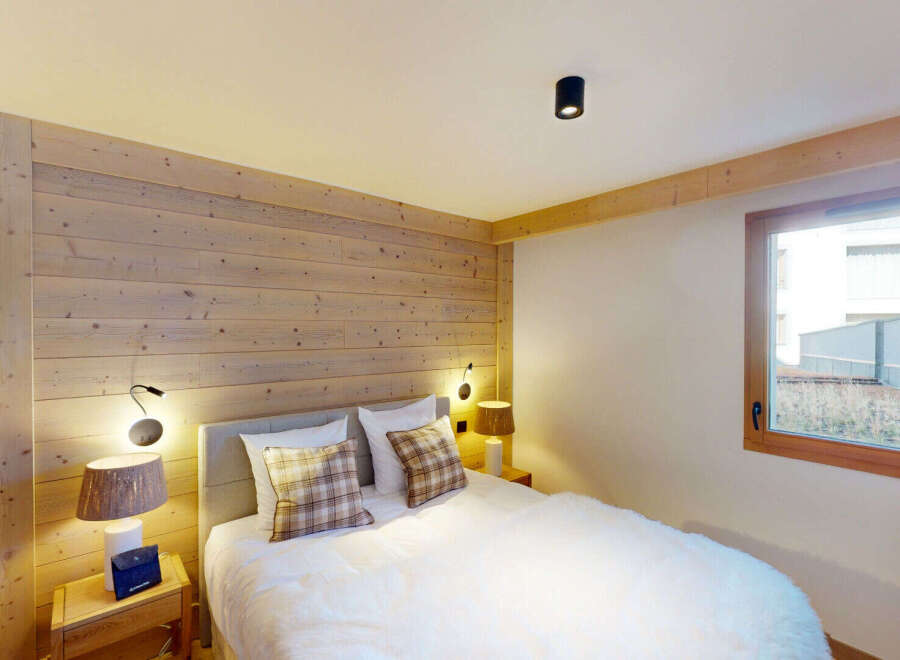 Experience cozy mountain living in this charming bedroom featuring warm, natural wood paneling on the walls and ceiling beams.