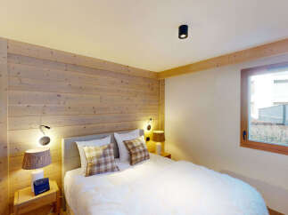 Experience cozy mountain living in this charming bedroom featuring warm, natural wood paneling on the walls and ceiling beams.