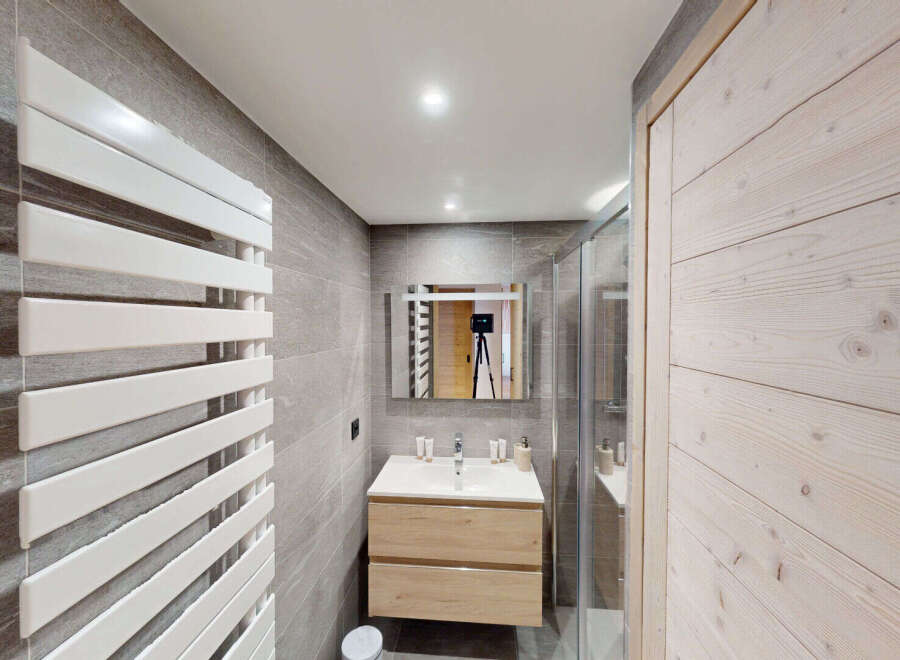 This modern bathroom features a sleek white towel warmer against a backdrop of elegant grey tiled walls.