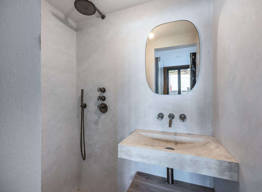 This modern bathroom showcases a minimalist design with a concrete sink and a unique, rounded mirror.