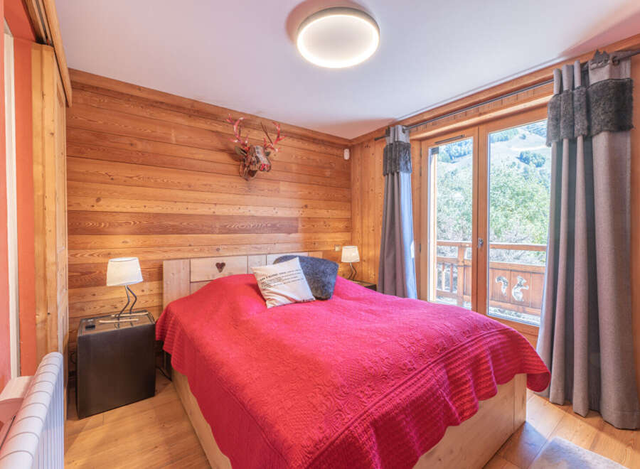 Experience the charm of this cozy bedroom featuring rustic wooden walls and a comfortable bed with a vibrant red cover.