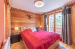 Experience the charm of this cozy bedroom featuring rustic wooden walls and a comfortable bed with a vibrant red cover.