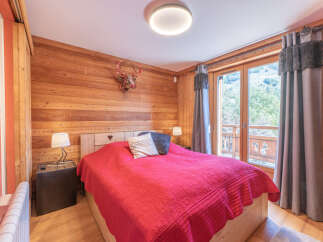 Experience the charm of this cozy bedroom featuring rustic wooden walls and a comfortable bed with a vibrant red cover.