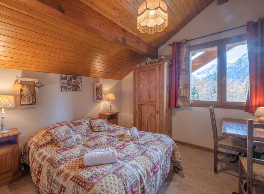 This charming bedroom features a cozy, rustic design with a wooden ceiling and a comfortable bed.