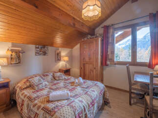This charming bedroom features a cozy, rustic design with a wooden ceiling and a comfortable bed.