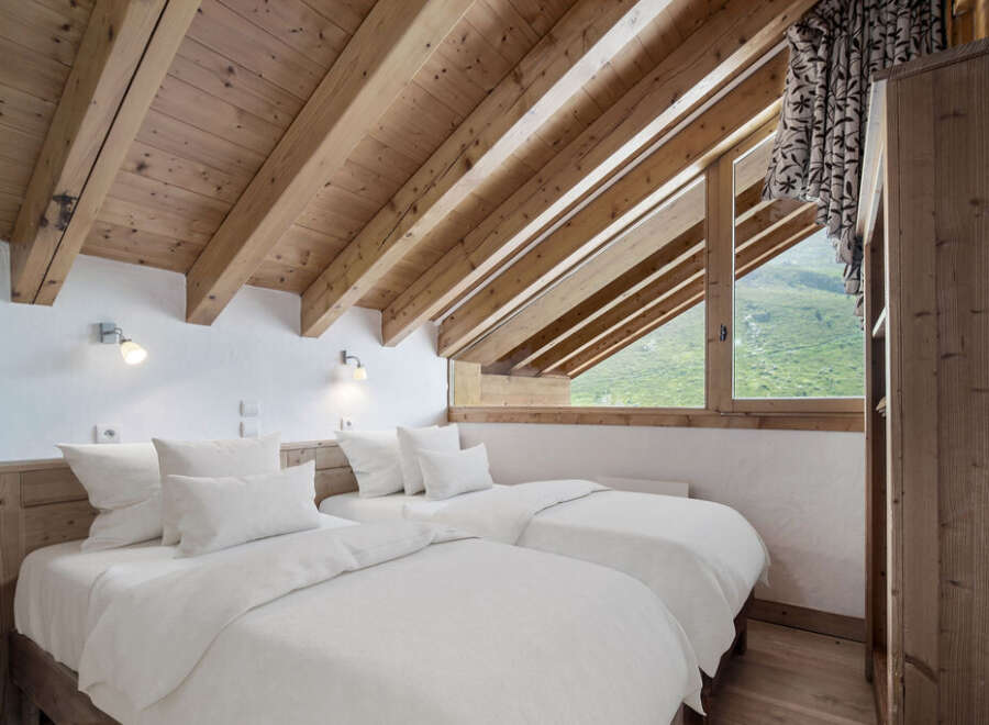 This cozy bedroom features a unique sloped ceiling with exposed wooden beams, creating a warm and inviting atmosphere.