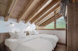 This cozy bedroom features a unique sloped ceiling with exposed wooden beams, creating a warm and inviting atmosphere.