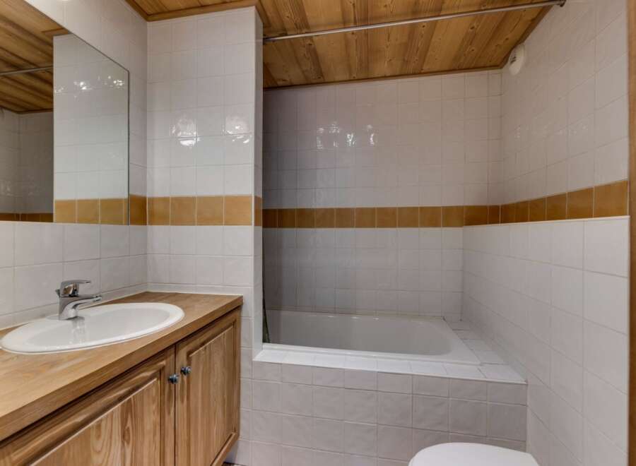 This bathroom features a clean and modern design with white tiles and a wooden vanity.